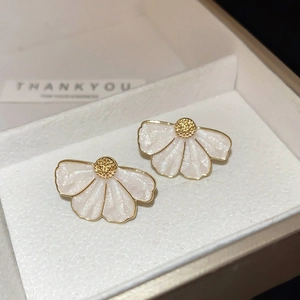 Détail macro de boucles d'oreilles fleurs blanches et dorées sur boîte à bijoux texturée