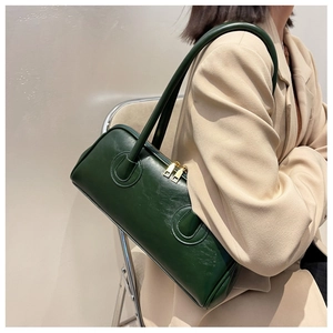Detail of dark green cylindrical shoulder bag in glossy faux leather worn by a model