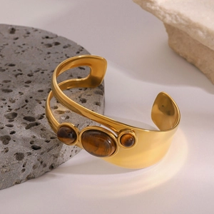 Detail of gold open bangle featuring three polished tiger eye stones on textured stones