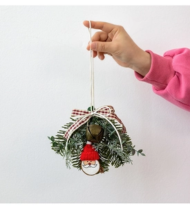 Detail of Christmas ornament featuring Santa wood slice, pine needles, and bronze bell
