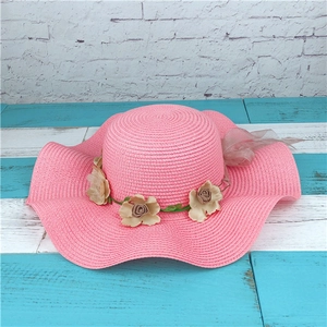 Detailed view of the wide wavy brim and floral decor on this pink straw sun hat