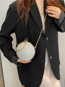 Sparkling silver spherical evening bag with gold ring handle and chain strap on black suit