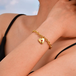 Dettaglio di un bracciale a catena dorata con ciondolo a cuore e pietra rossa incastonata