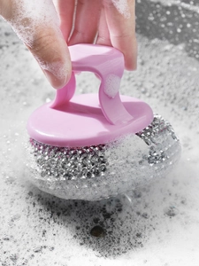 Close-up of pink handle steel wire brush cleaning soapy surface with thick foam