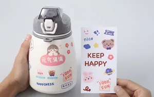 Dettaglio di simpatici adesivi cartoon su una borraccia bianco latte con cannuccia