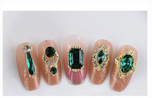 Macro detail of emerald green gemstones with gold setting on manicured nail tips