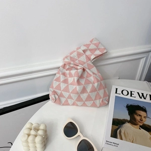 Close-up of pink and white geometric triangle knit wrist bag with minimalist accessories