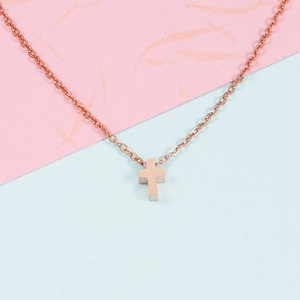 Détail d'un petit pendentif croix en or rose sur une fine chaîne maille jante