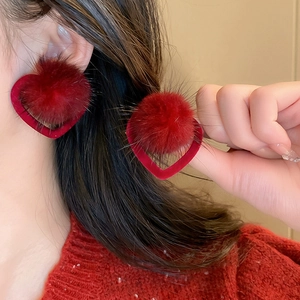 Detail view of red heart earrings with fluffy pom-poms and velvet texture on ear