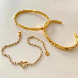 Detail von goldenem Herz-Armband und gehämmertem Edelstahl-Armreifen-Set im Stapel-Look