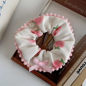 Detail of plush beige hair scrunchie with pink strawberry print and fuzzy trim