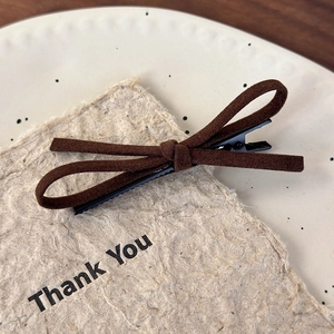 Close-up of a dark brown suede bow hair clip with a jagged metal duckbill grip