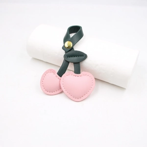 Detail of pink heart-shaped leather cherry bag charm with green leaf and golden snap