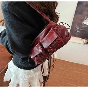 Close-up of wine red pleated shoulder bag with long decorative ribbons on leather