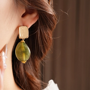 Close-up of square gold metal and green drop pendant earring worn by a model