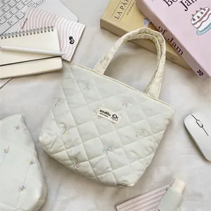 Quilted off-white canvas tote with bow embroidery and brand label on a desk