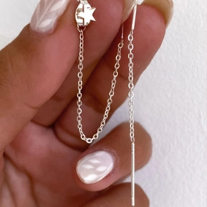 Detail showing long silver chain earrings with star charms held against a white background