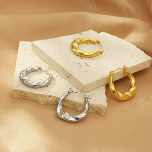 Detailed shot of gold and silver twisted hoop earrings on stone and beige silk