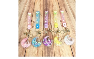 Flat lay view of five colorful moon-shaped liquid quicksand keychains on wood background