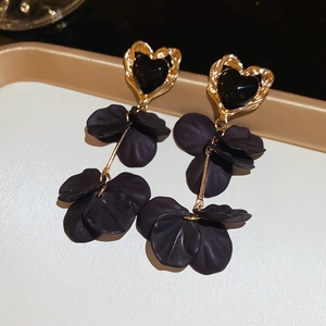 Detail view of long heart and black petal tassel earrings on a decorative tray