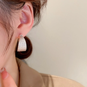 Close-up of curved silver textured earrings worn on a model against a beige background