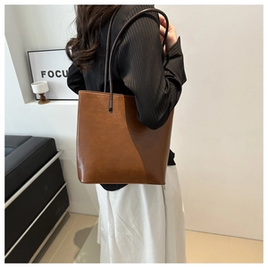 Detail of a vintage brown leather tote bag worn on shoulder by a model in a modern room