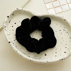 Close-up of a premium black velvet hair scrunchie on a white textured ceramic dish