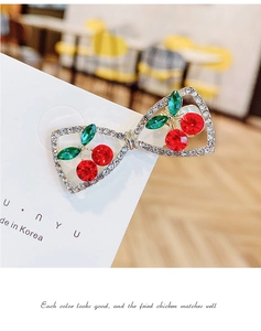 Detailed close-up of a bow hair clip with red cherry rhinestones on a display card