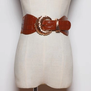 Detail of brown faux crocodile leather wide belt with decorative gold buckle on a mannequin