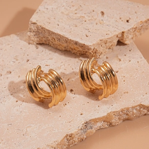 Detail view of gold triple-layered C-shape geometric earrings on a natural stone base