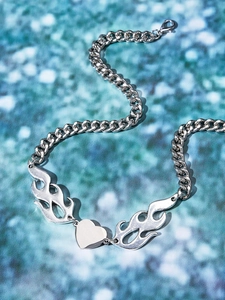 Detail shot of a silver heart pendant with flame pattern and chunky curb chain on blue glitter