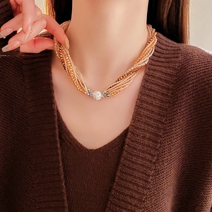 Détail d'un collier de perles multicouches avec fermoir magnétique sur un pull marron