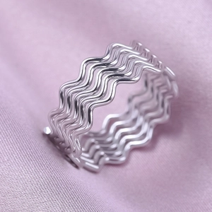 Macro detail of silver wavy stainless steel ring with polished finish on purple fabric