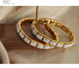 Dettaglio di due bracciali a maglie dorate con micro-pavé di zirconi bianchi su fondo in seta