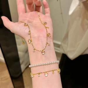 Detail of pink heart pendants and pearl bracelet set on wrist with golden metal finish