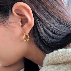 Close-up of elegant gold twisted rope hoop earrings worn on a model's ear