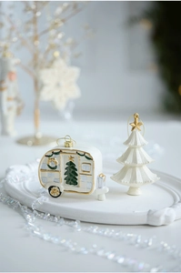 Detail of ceramic Christmas caravan and tree ornaments with gold hooks on a white tray