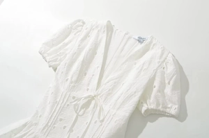 Détail de la broderie ajourée blanche sur robe à col en V avec taille à cordon serrage