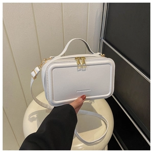 Close-up of a white leather suitcase bag featuring golden zippers and embossed frame details