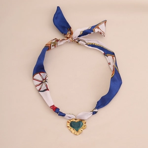 Silk scarf necklace with golden heart pendant and green gemstone on beige background