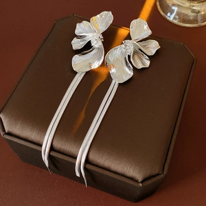 Makroaufnahme von silbernen Blumenohrringen mit langen Quasten auf einer Lederbox