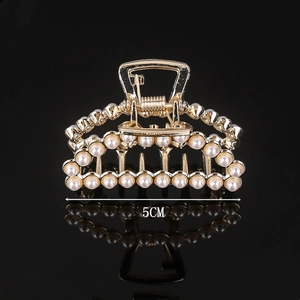 Detailed view of 5cm golden hair claw clip with pearls on black reflective surface