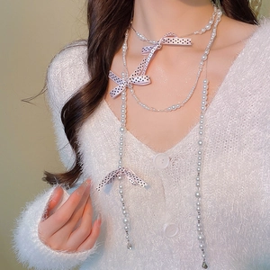 Detail of multi-layer pearl necklace with pink ribbon bows on a model wearing a white cardigan