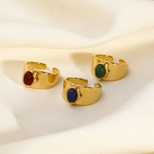 Detailed close-up of wide gold-plated steel rings with red, blue, and green oval gemstones