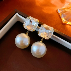 Macro shot of square crystal and white faux pearl drop earrings with gold-tone settings