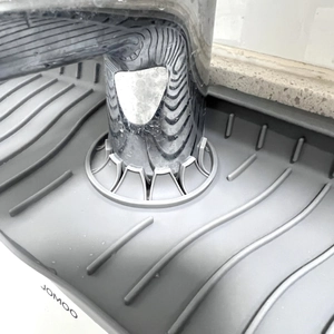 Close-up of grey silicone faucet splash guard with wave drainage pattern and water drops