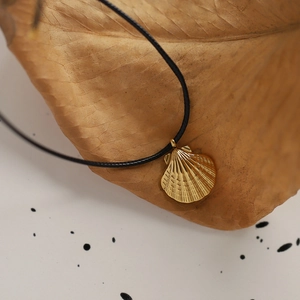 Macro shot of gold shell pendant on black cord necklace styled on a dried leaf background