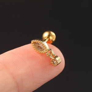 Macro view of a gold-tone stainless steel ear stud with zircon held on a fingertip