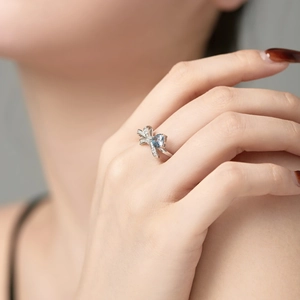 Close-up of elegant S925 silver bow ring with blue pear-cut stone on a model's hand