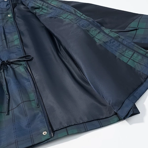 Détail d'un manteau à carreaux avec motif bleu-vert, fermeture éclair et cordon serrage